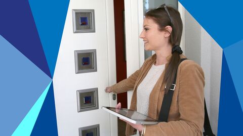 Junge frau mit Tablet in der Hand steht vor einer Haustüre.