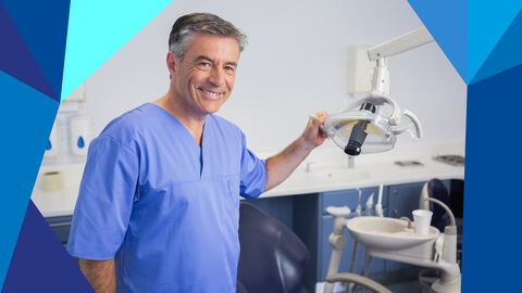 Zahnarzt im Justizvollzug Zahnarzt steht vor dem Behandlungsstuhl und hält sich mit der linken Hand an der Lampe fest.